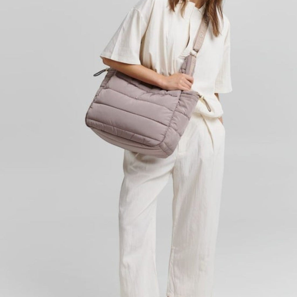 A woman wearing a beige Lieblingstasche Alltime Buddy quilted shoulder bag with a matching branded strap