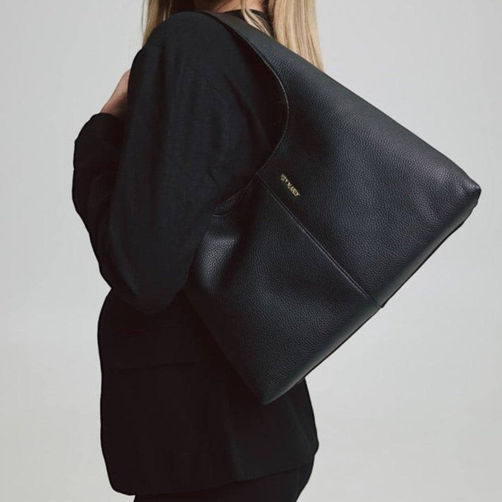 Lieblingstasche Alltime Lover M black leather hobo bag worn over the shoulder by a blonde woman in a black blazer