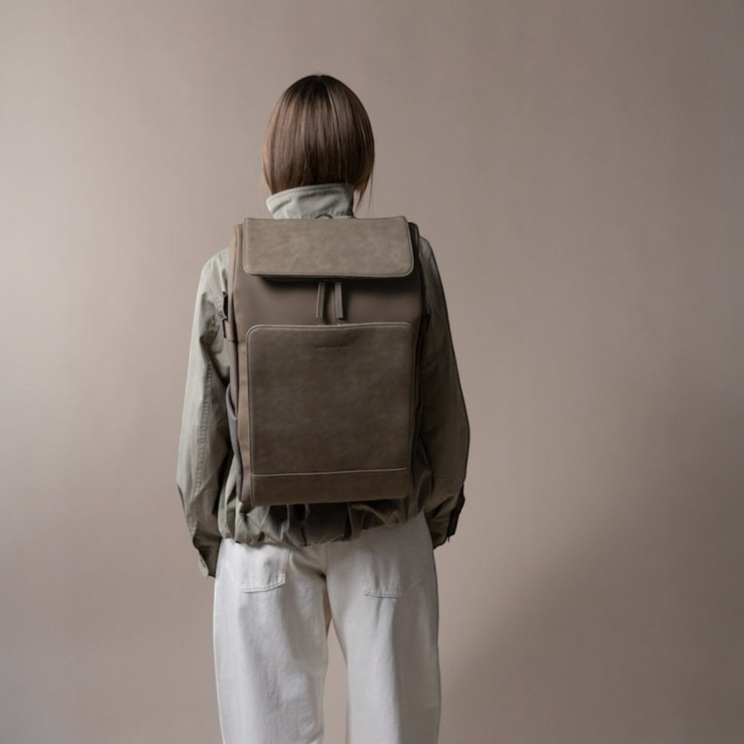 Lieblingstasche Bali Pro taupe faux leather backpack with flap closure and front pocket, worn by a person from behind.