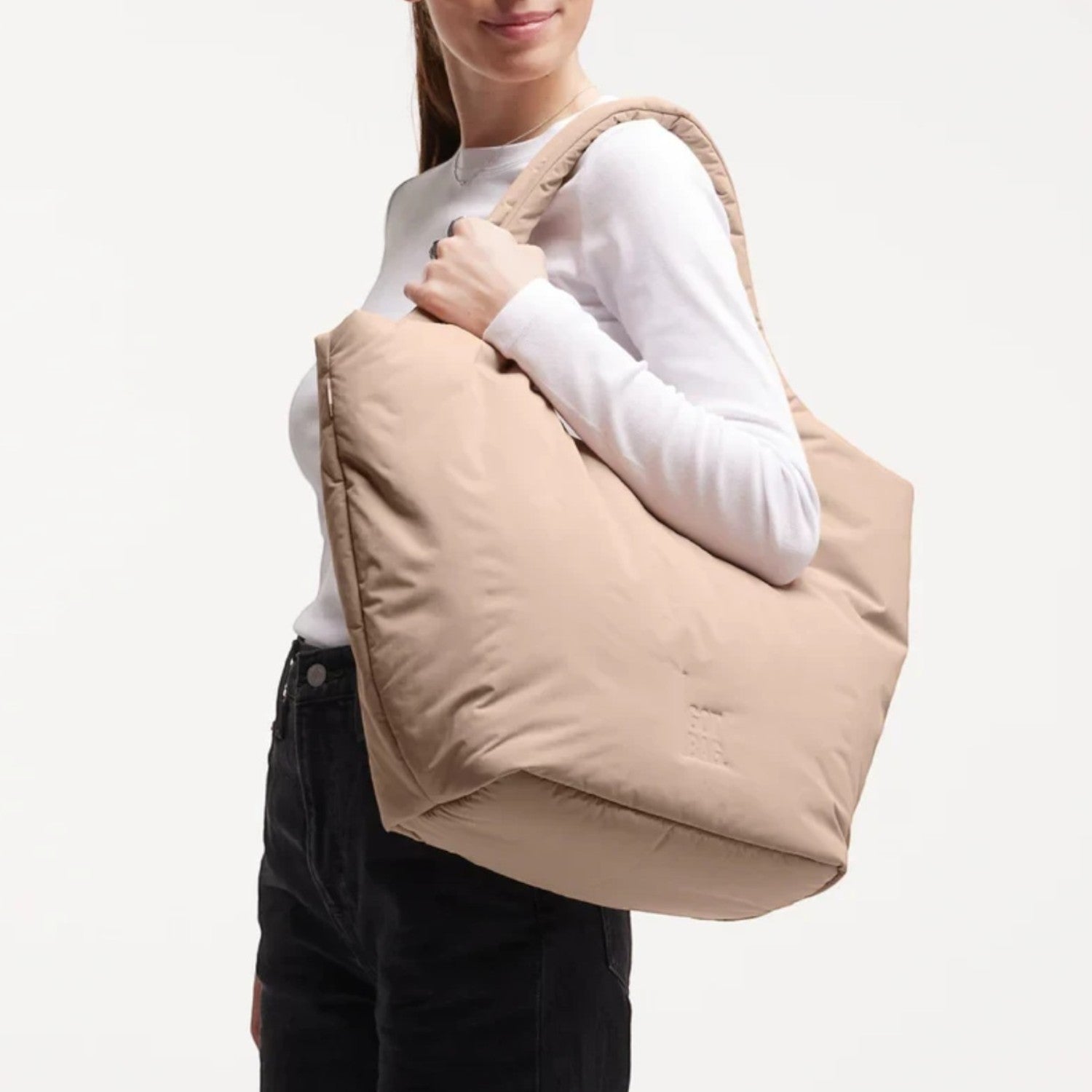 A model wearing a beige Lieblingstasche Cloud Tote Bag made from water-resistant RE:NYNET material over her shoulder.