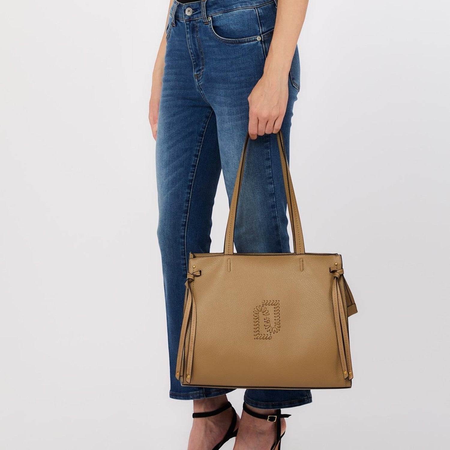 Lieblingstasche Tote L in beige leather with side tassel details and embossed logo, held by a woman in blue jeans.