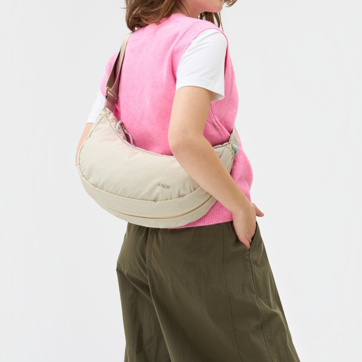 A woman wearing a beige Lieblingstasche sling bag over her shoulder with a pink vest and olive green trousers.