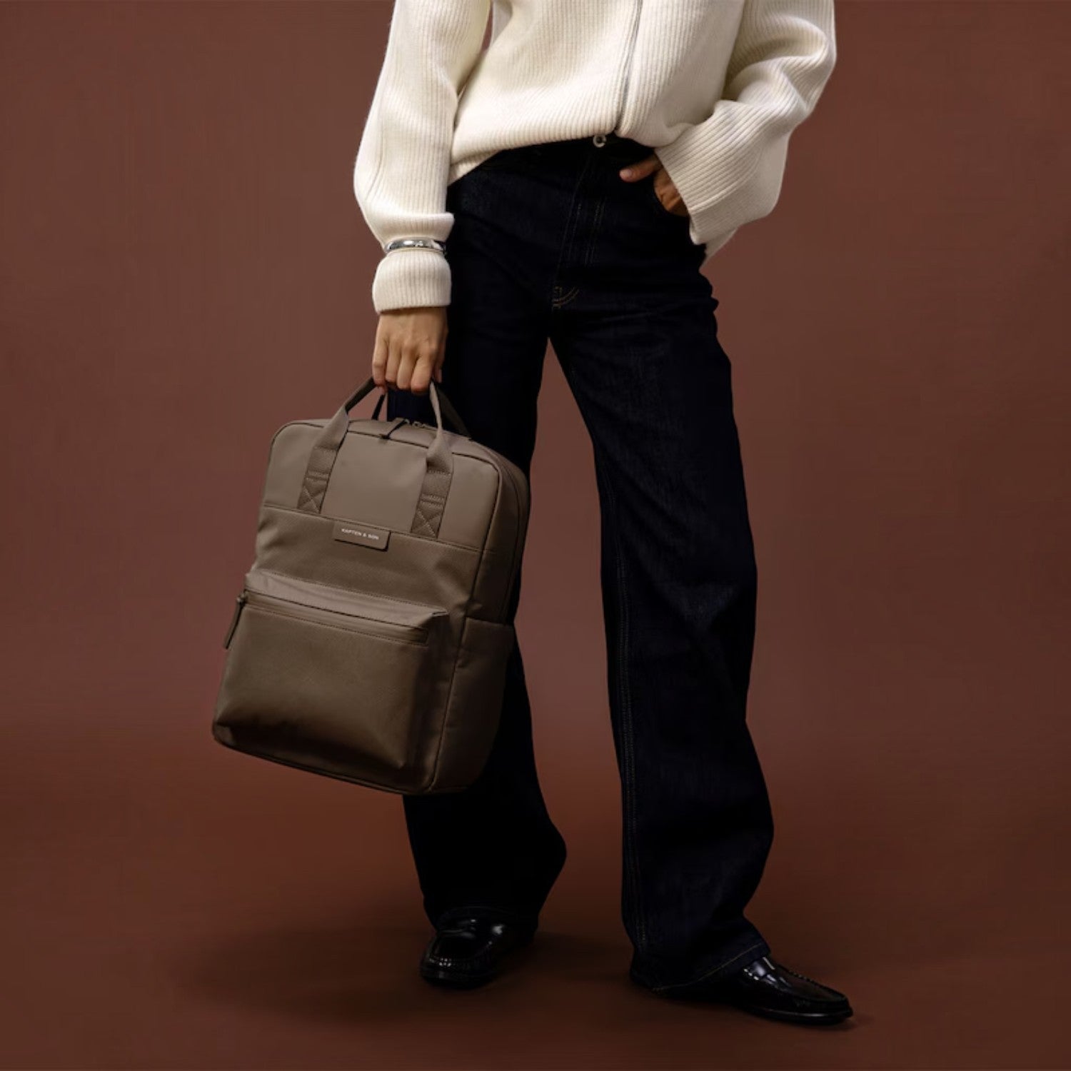 Lieblingstasche Kapten & Son Bergen Pro backpack in taupe held by a person wearing a white sweater and dark jeans