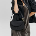 Lieblingstasche Big Sister black pebbled leather crossbody bag worn by a woman in a black jacket and satin dress