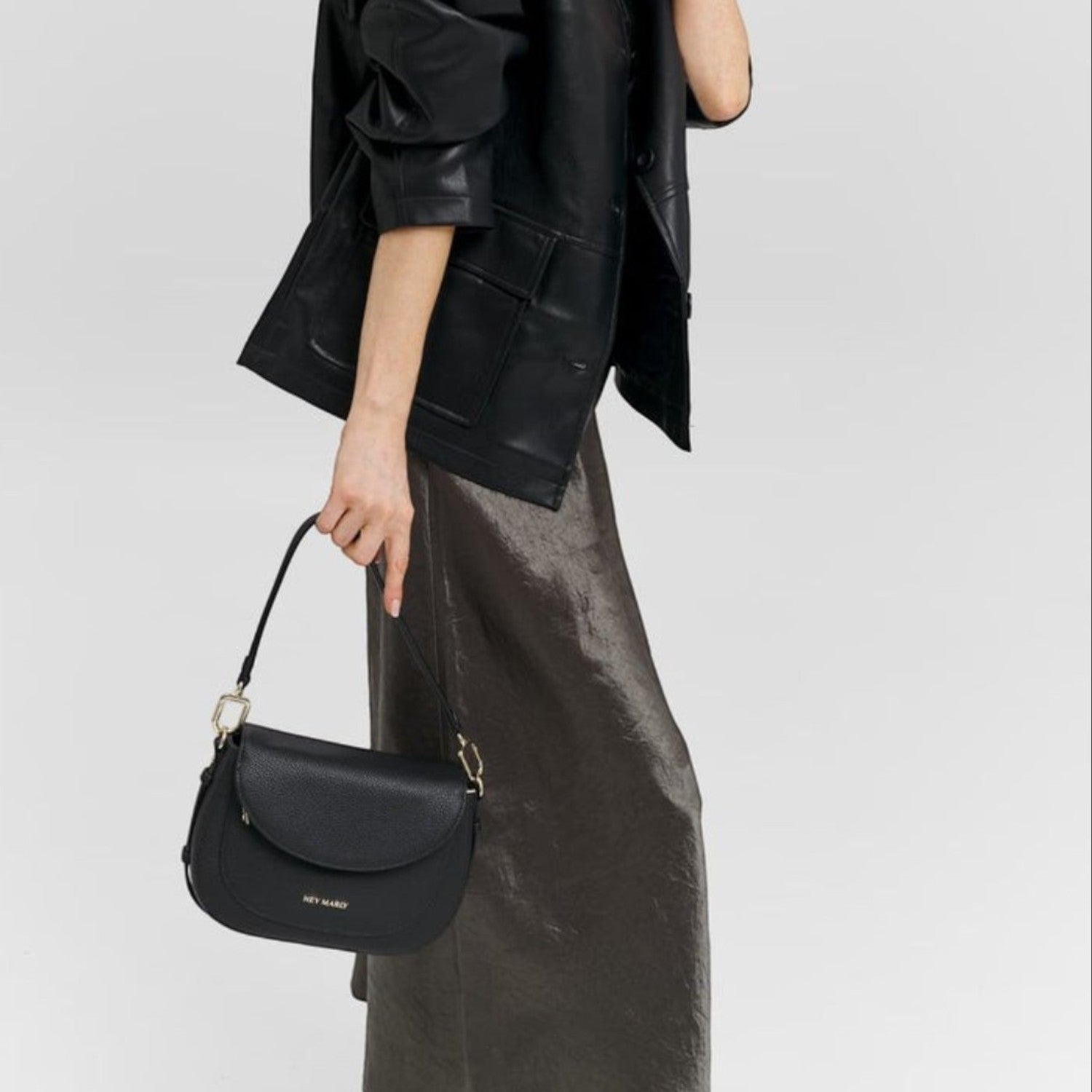Lieblingstasche Big Sister black leather shoulder bag with gold hardware held by a model in a black leather jacket