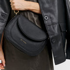 Lieblingstasche Big Sister black pebbled leather crossbody bag with gold hardware worn over a dark dress and jacket