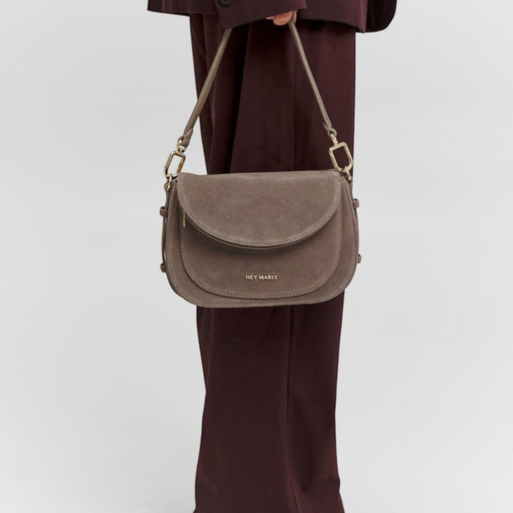 Lieblingstasche Big Sister Suede taupe shoulder bag with gold hardware held by a person in a dark burgundy suit