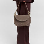 Lieblingstasche Big Sister Suede taupe shoulder bag with gold hardware held by a person in a dark burgundy suit