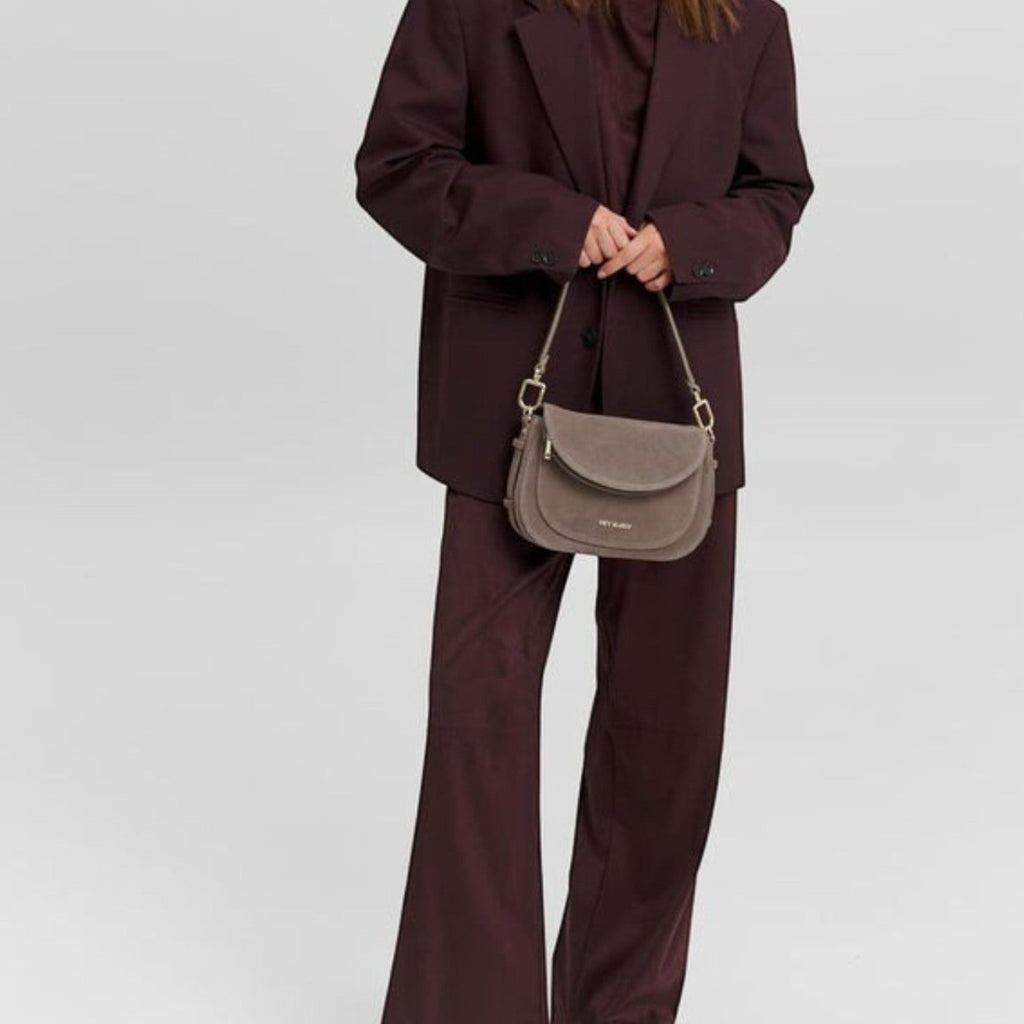 Model wearing a dark burgundy suit carrying a taupe suede Big Sister Suede handbag by Lieblingstasche