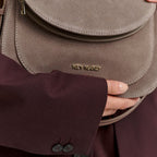 Lieblingstasche Big Sister taupe suede crossbody bag with gold logo hardware held by a person in a dark blazer