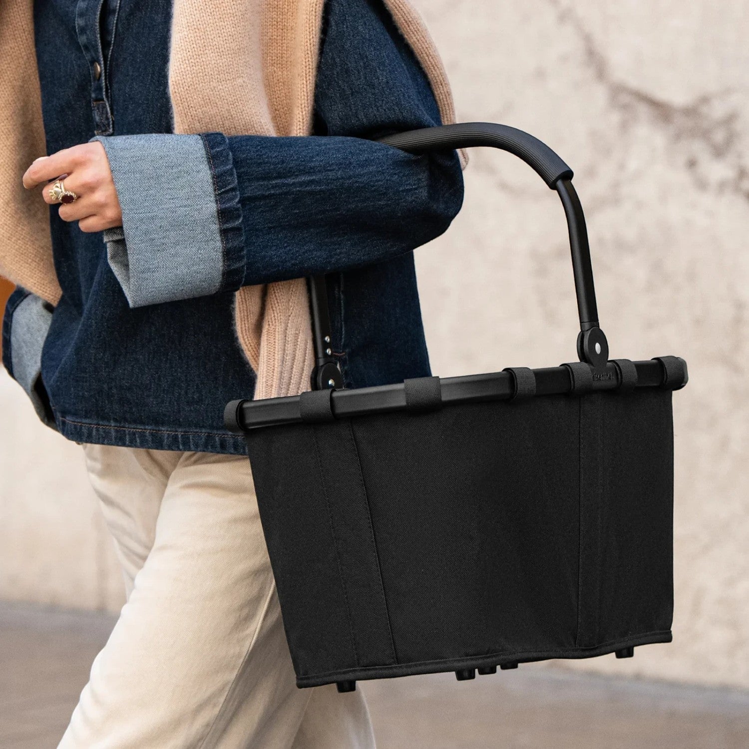 Lieblingstasche Carrybag in black with a sturdy aluminium handle, held by a person wearing a denim jacket.