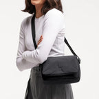 Woman smiling while wearing a black Lieblingstasche Cloud Crossbody Bag made of water-resistant RE:NYNET material.