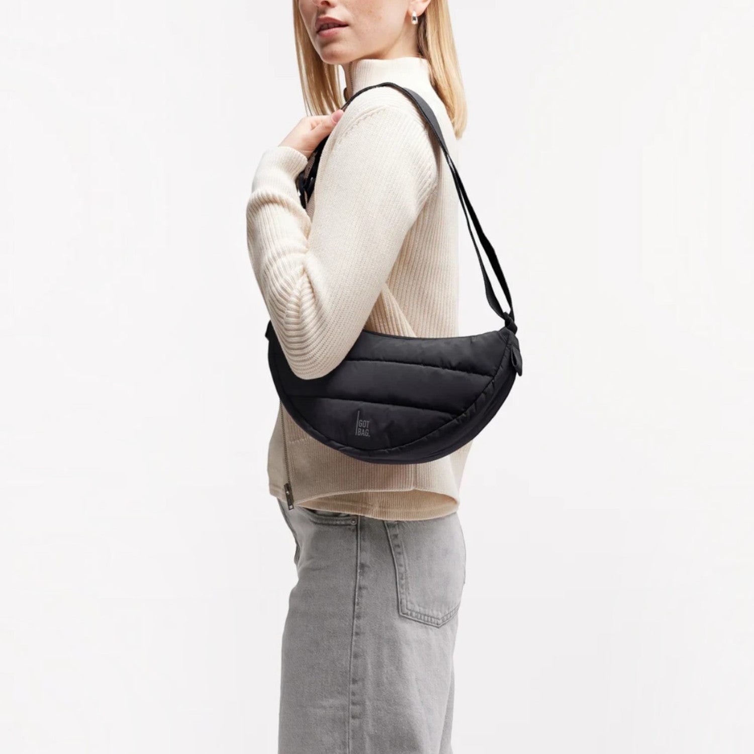 Lieblingstasche Puffer Moon Bag Small in black, worn as a crossbody bag by a woman in a cream sweater.