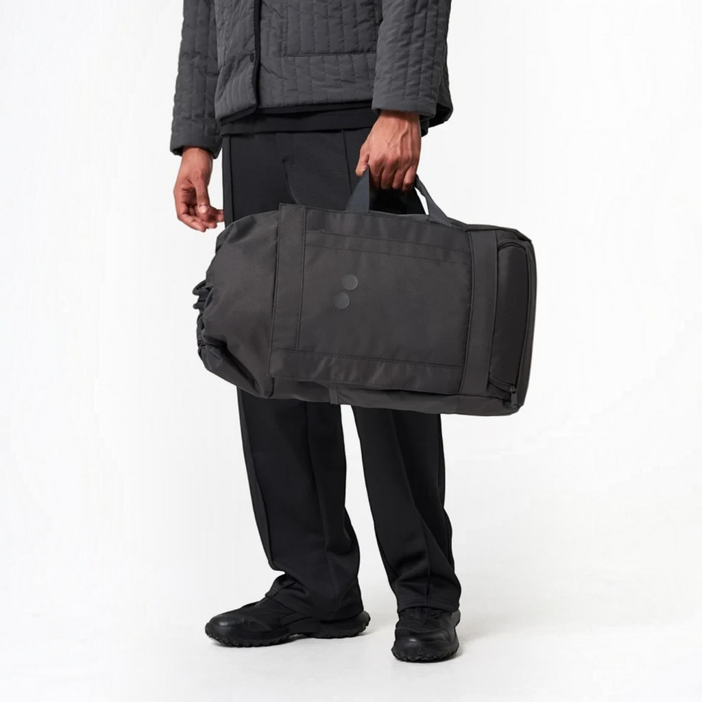 Lieblingstasche Blok Medium charcoal grey duffel bag held by a person wearing matching dark casual clothing