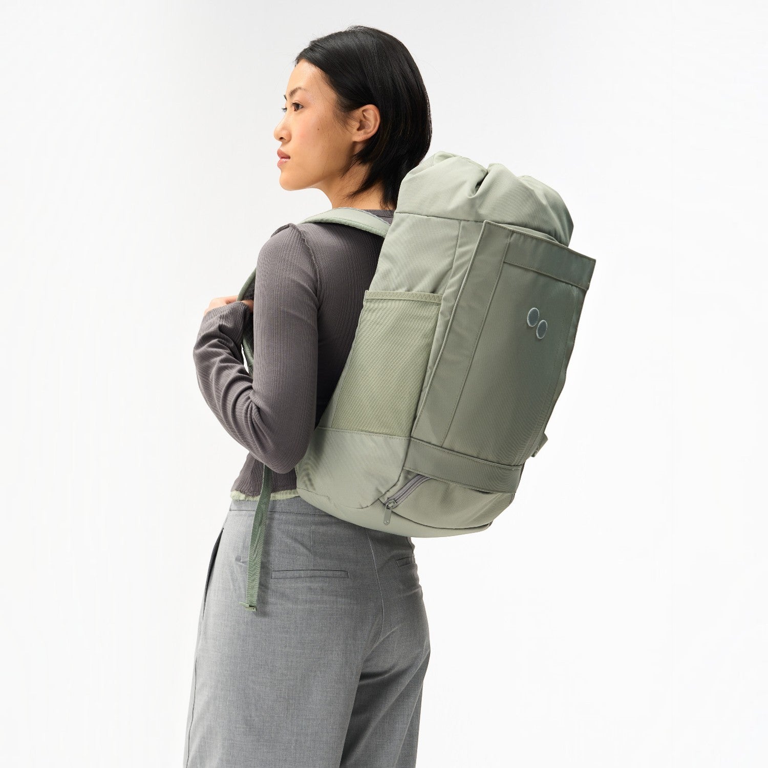Lieblingstasche Blok Medium sage green backpack worn by a woman, featuring side mesh pockets and a roll-top design.
