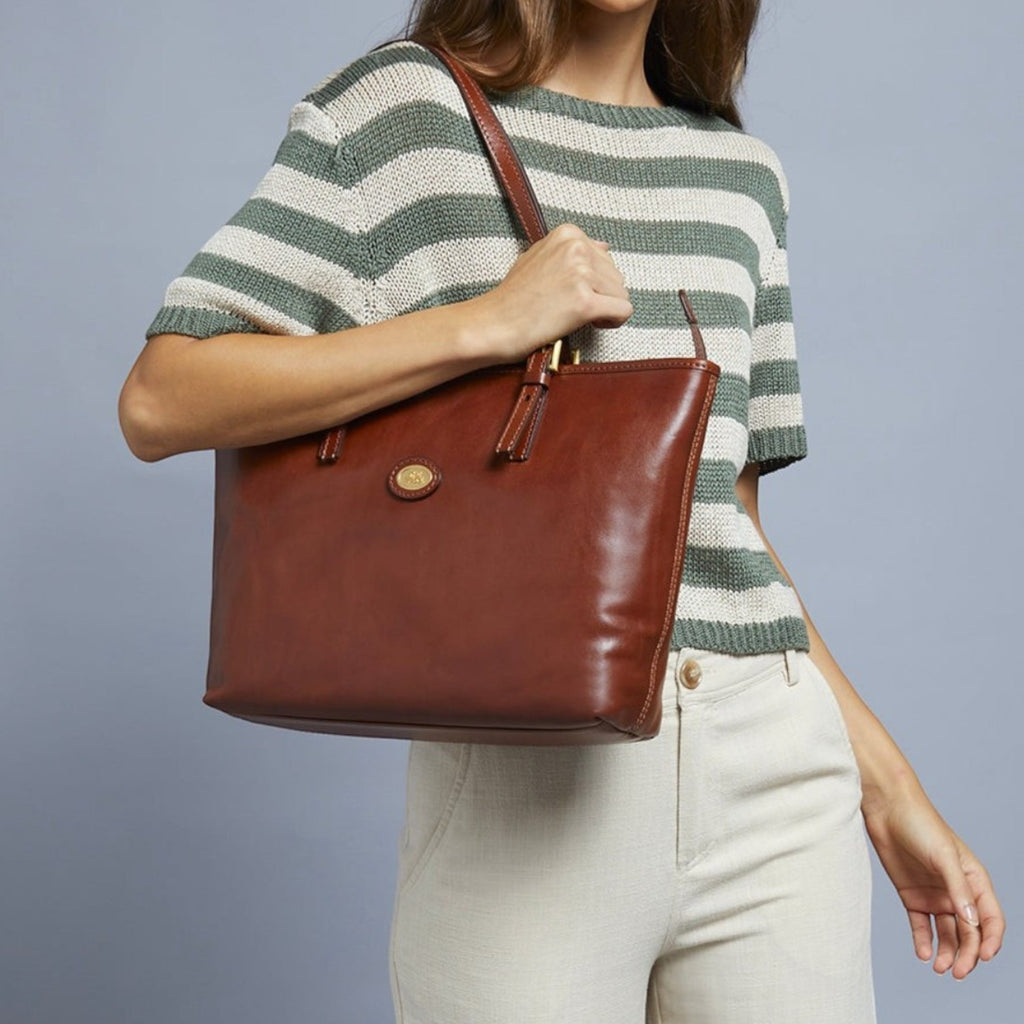 Lieblingstasche brown leather shopper bag with zipper and gold hardware, held by a woman wearing a striped green and white top.