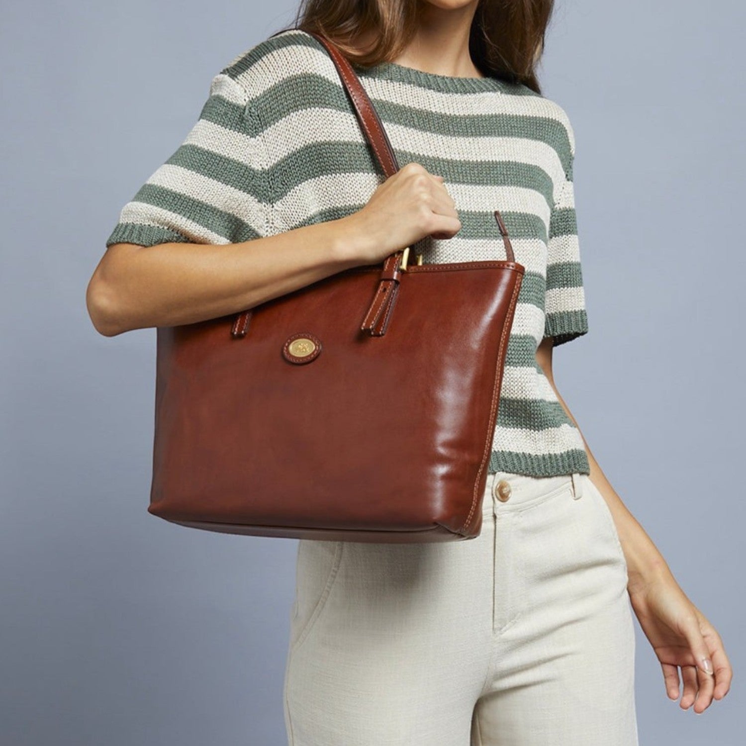 Lieblingstasche brown leather shopper bag with zipper and gold hardware, held by a woman wearing a striped green and white top.