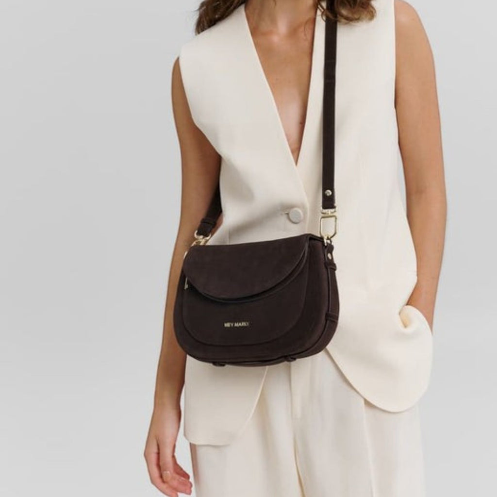 Woman wearing a dark brown suede Big Sister Suede crossbody bag by Lieblingstasche with a cream vest and trousers