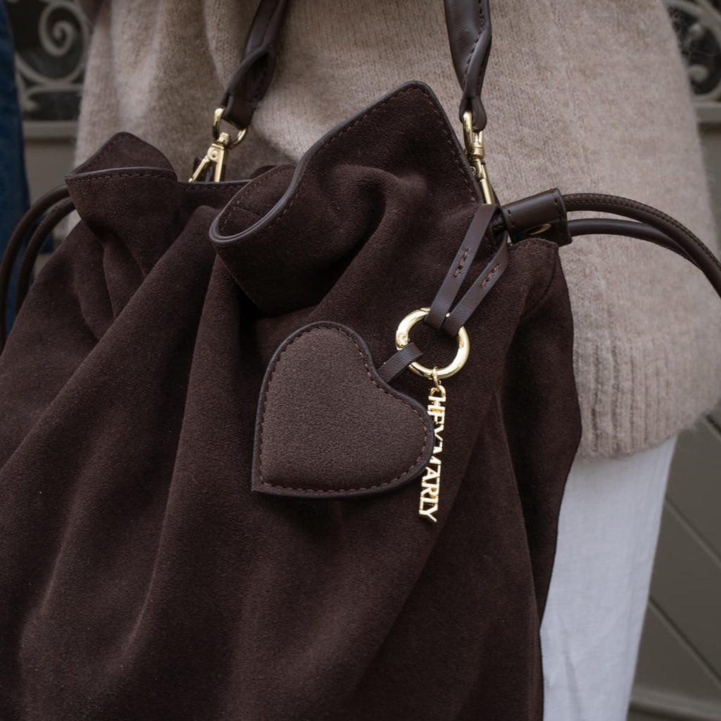 Lieblingstasche dark brown suede bucket bag with a heart charm and gold hardware worn by a person in a beige sweater