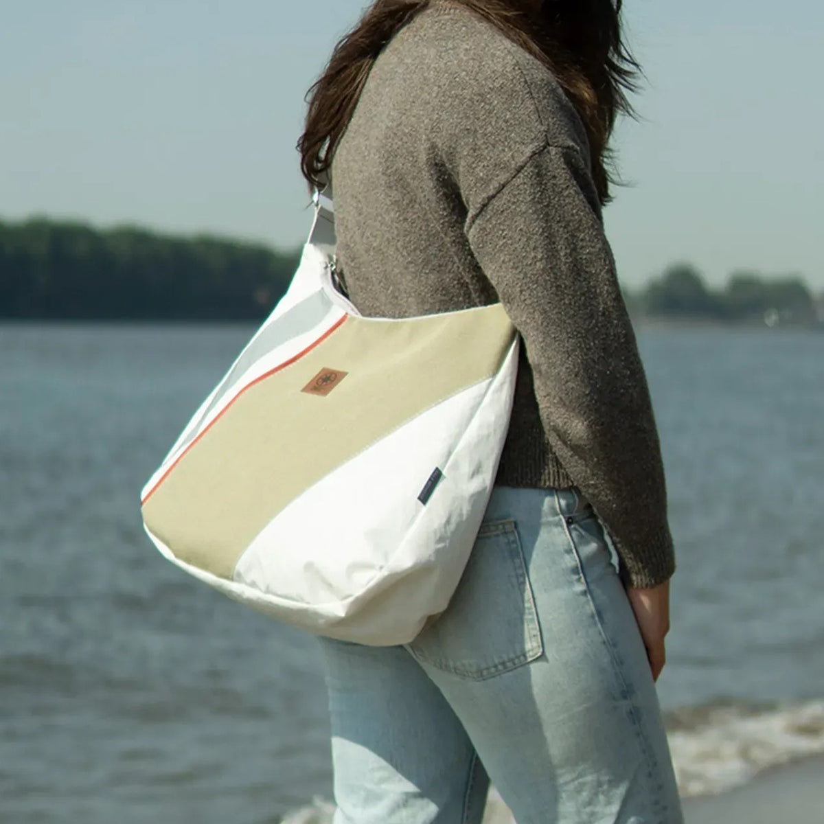 Lieblingstasche Bucht shoulder bag in white and beige with red accents worn by a woman at the beach