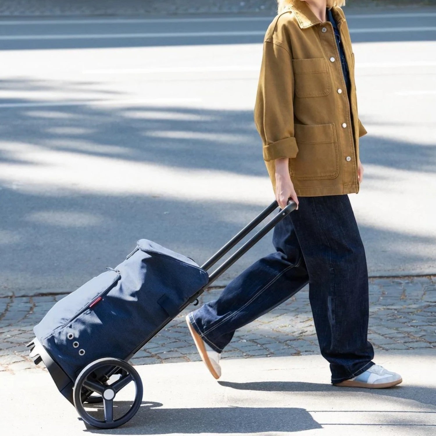 Lieblingstasche citycruiser bag in navy blue being pulled on a sidewalk by a woman in a brown jacket and jeans