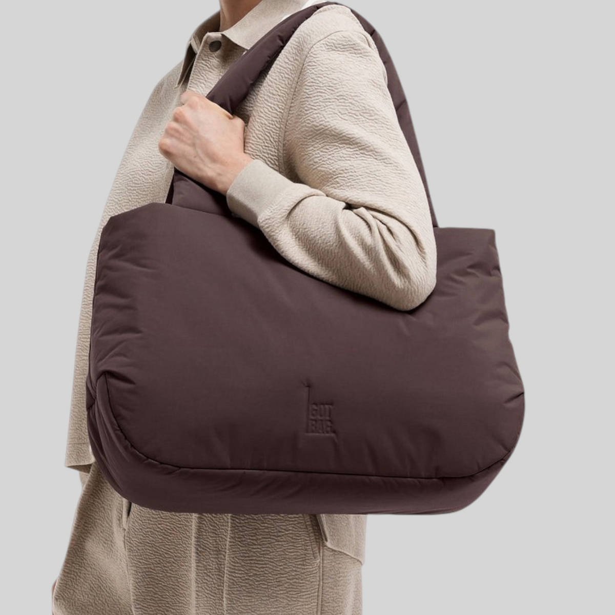 A woman smiling while carrying a Lieblingstasche Cloud Horizon tote bag in dark brown padded fabric on her shoulder.