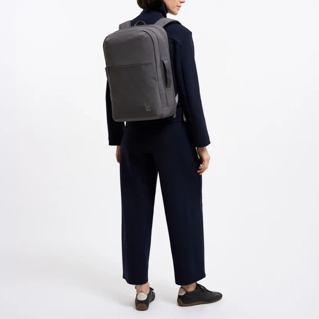 A woman wearing a grey Lieblingstasche Commuter Pack backpack while dressed in a dark navy professional outfit.