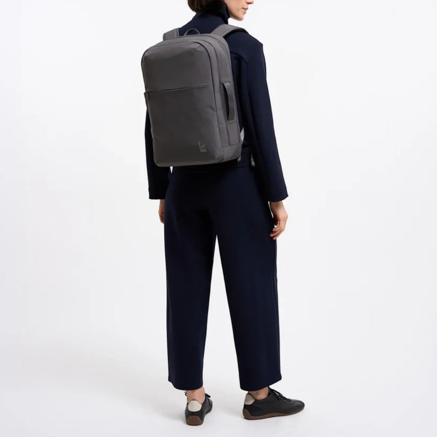 A woman wearing a grey Lieblingstasche Commuter Pack backpack while dressed in a dark navy professional outfit.