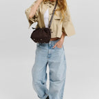 A woman wearing a Lieblingstasche Cool Companion Suede S dark brown suede crossbody bag with a drawstring closure.