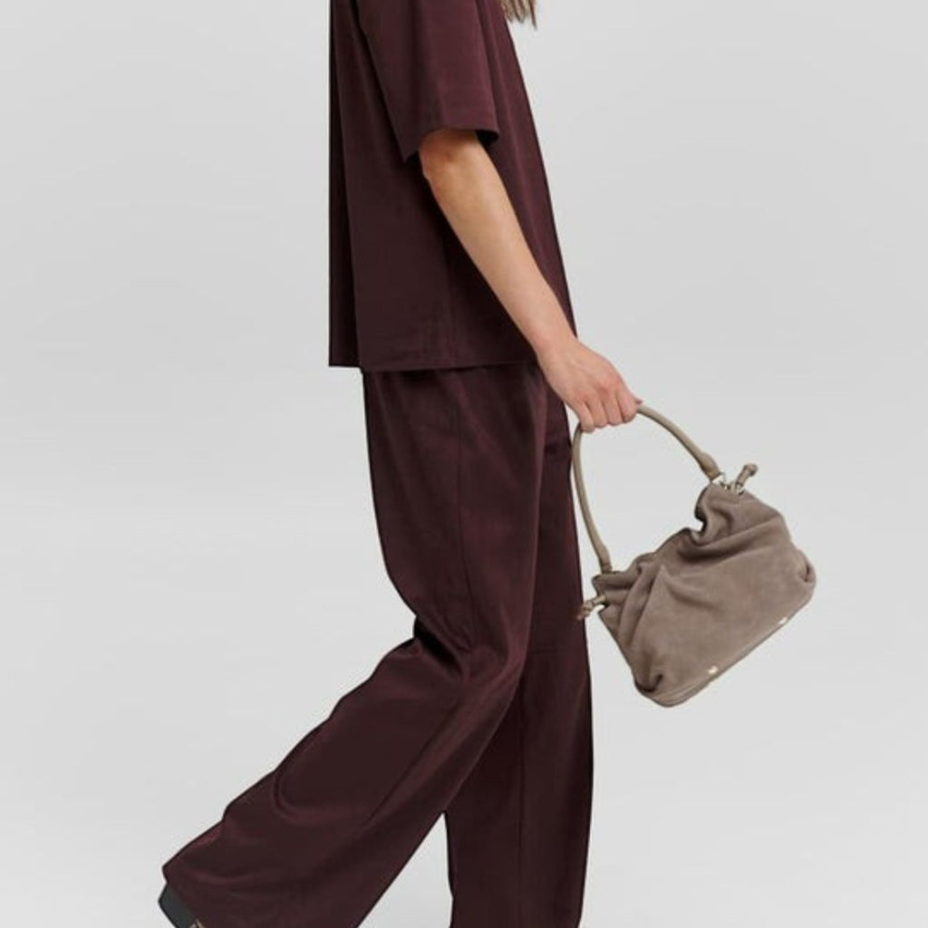 Lieblingstasche Cool Companion Suede S handbag in taupe held by a model wearing a dark burgundy matching set