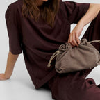 Lieblingstasche Cool Companion Suede S taupe suede drawstring pouch bag held by a woman in a dark brown outfit