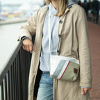 Lieblingstasche Deern Lütt crossbody bag in white, grey, and olive green with a striped accent worn by a woman