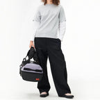 Lieblingstasche Duffel Pack in grey and black, held by a model wearing a grey t-shirt and black trousers.