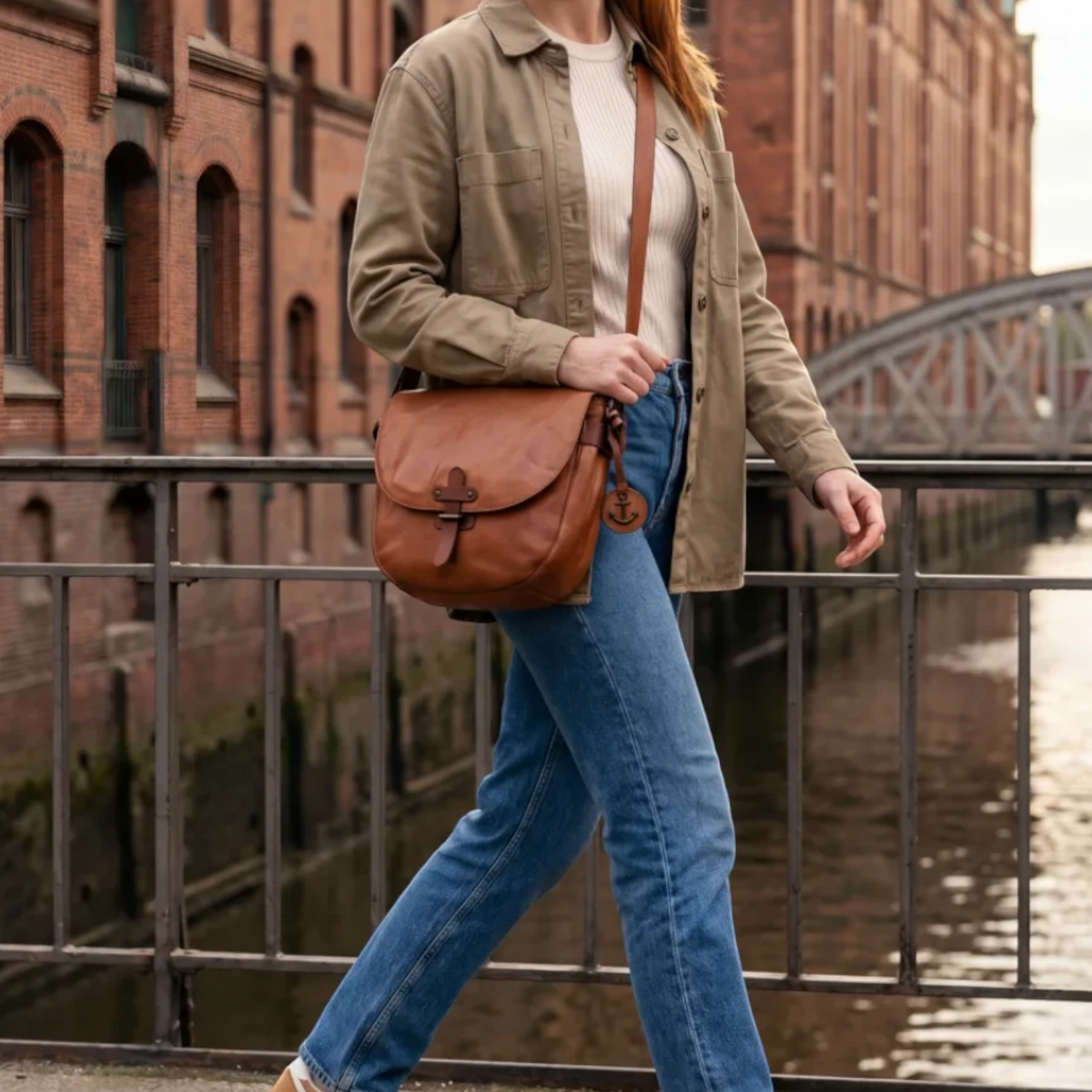 Woman wearing a Lieblingstasche Emmeline brown leather crossbody bag while walking across a city bridge