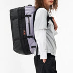 Model wearing a Lieblingstasche black and grey expandable duffel backpack with 47-60L capacity for travel and sports.