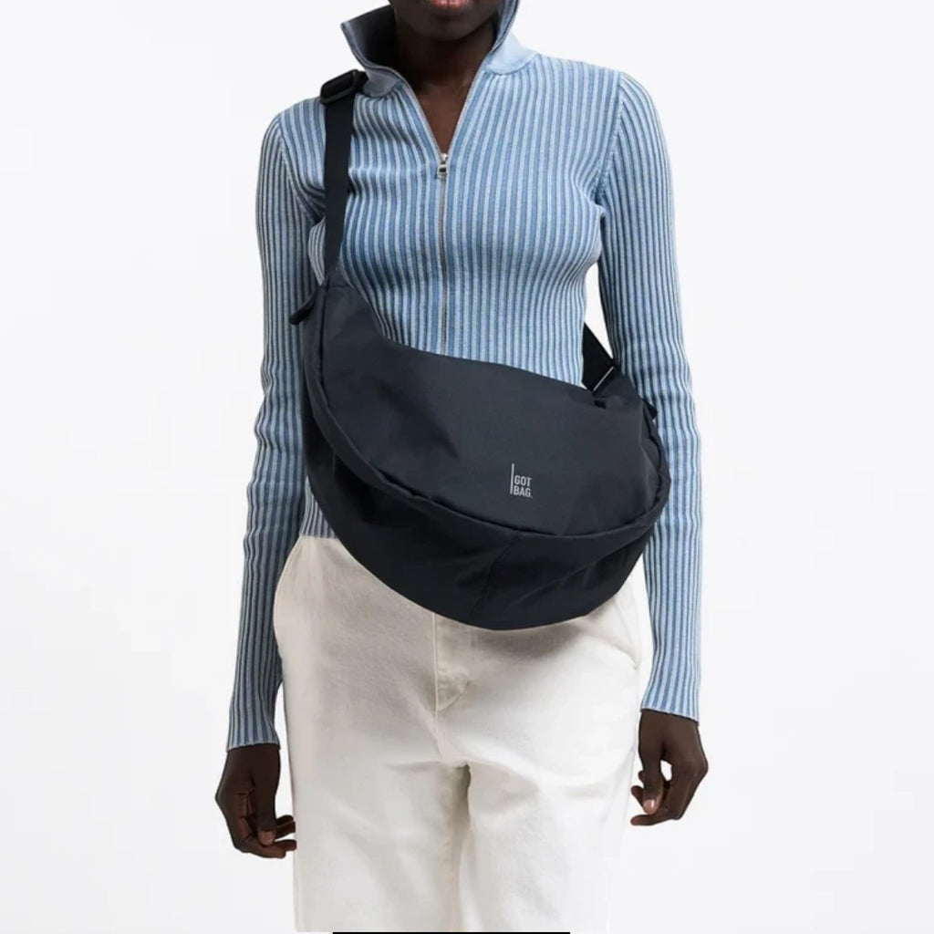 Model wearing a black GOT BAG Moon Bag Large crossbody, styled with a blue ribbed zip-up top from Lieblingstasche.