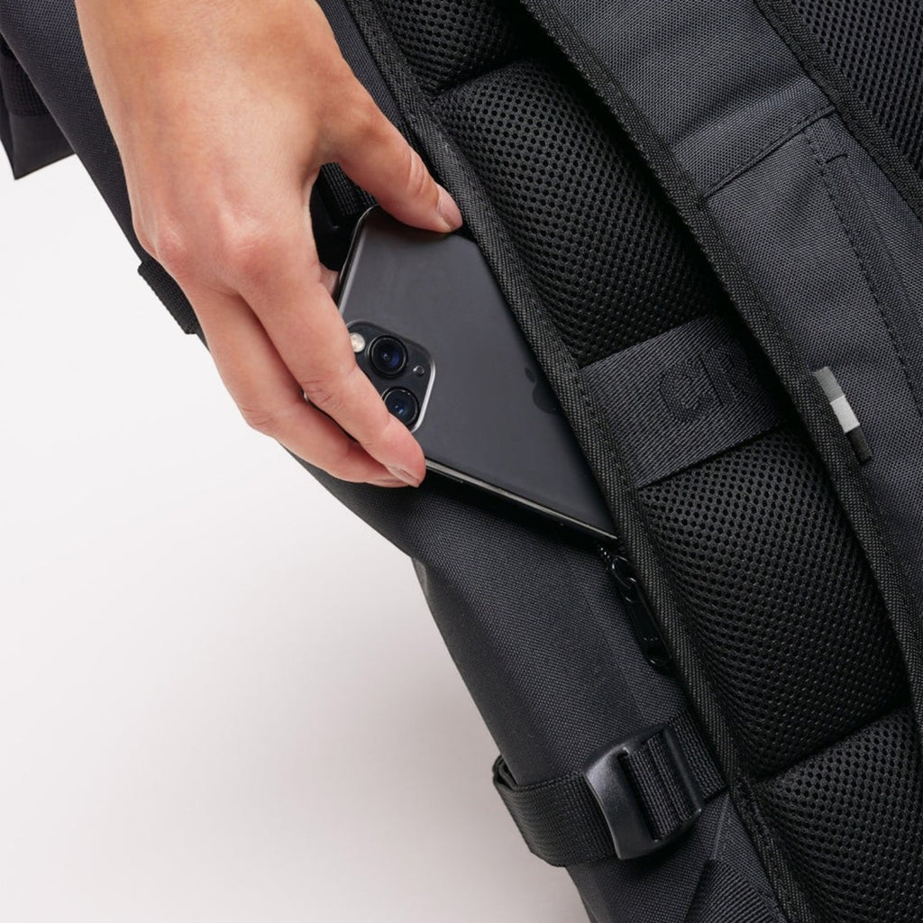 Lieblingstasche GOT BAG Rolltop 2.0 black backpack showing a hand placing a smartphone into a side zipper pocket