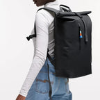 Model wearing a black Lieblingstasche GOT BAG Rolltop Lite 2.0 backpack with magnetic closure and adjustable straps.