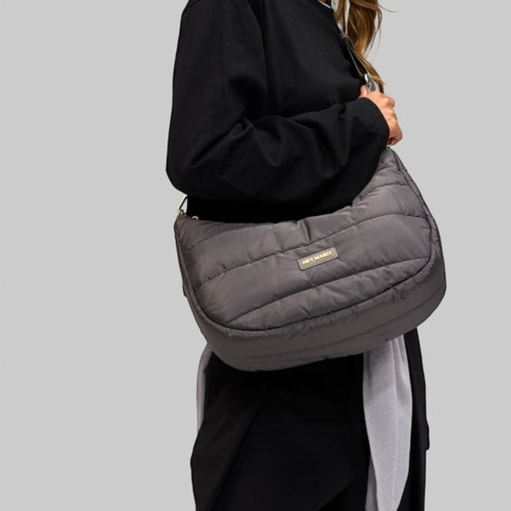 A woman wearing a dark grey quilted Lieblingstasche Lifetime Buddy M shoulder bag against a neutral background.