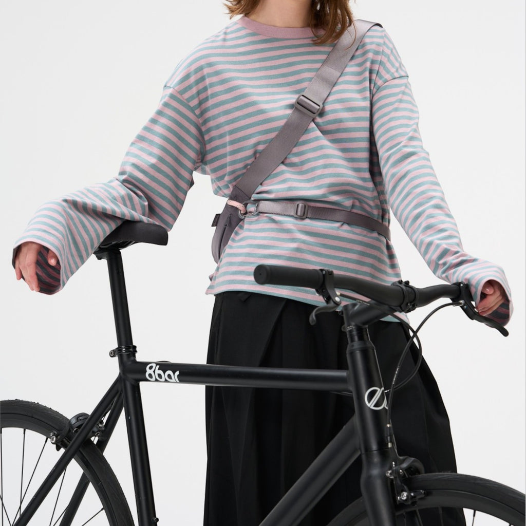 Lieblingstasche grey sling bag worn across the chest by a woman in a striped long-sleeve shirt with a black bicycle