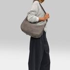 A woman wearing a grey Lieblingstasche Lifetime Sister suede shoulder bag with buckle details on a neutral background
