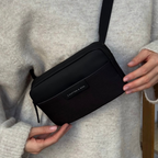 Lieblingstasche Habo compact black crossbody bag with a minimalist design worn by a person in a beige sweater