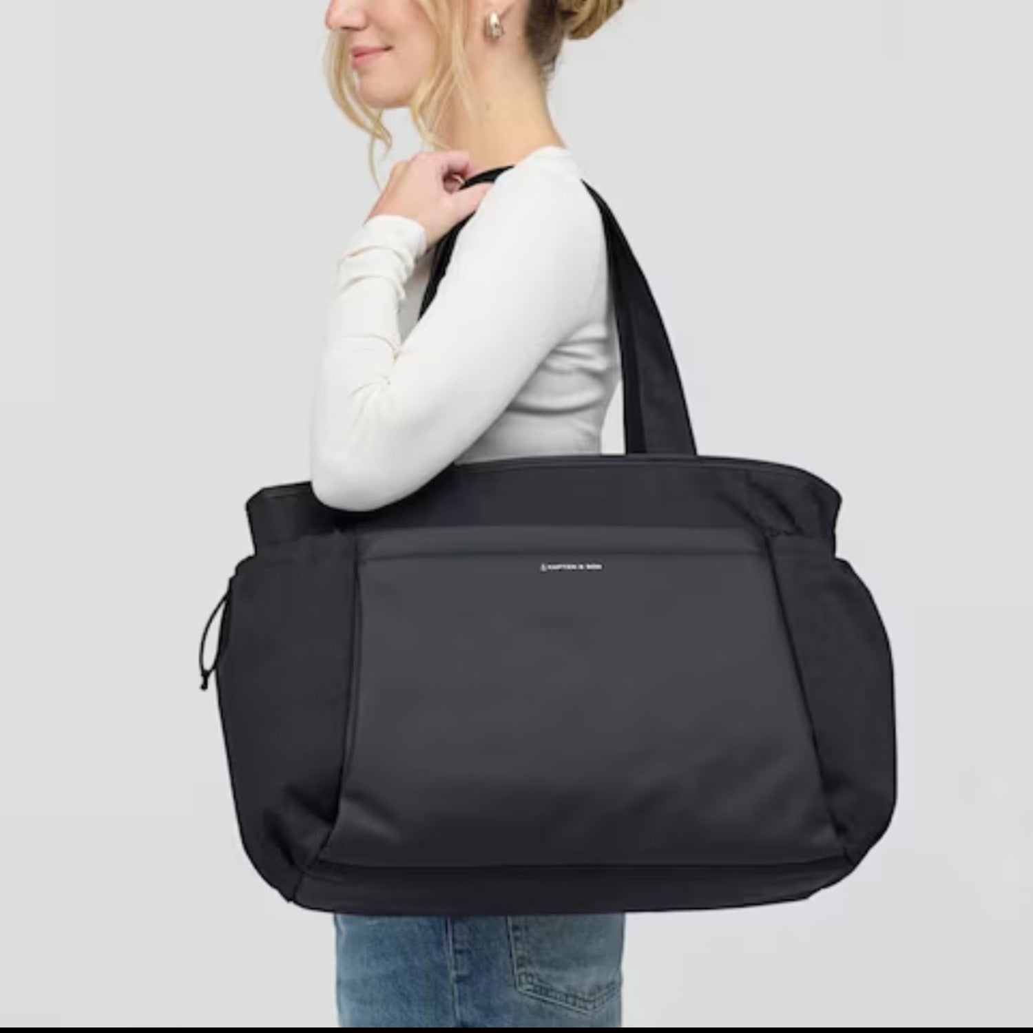 Woman carrying a black Lieblingstasche Hellvi Pro Large tote bag over her shoulder against a light grey background