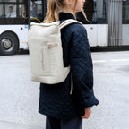 Lieblingstasche Helsinki backpack in off-white with a roll-top design, worn by a woman in a black quilted jacket.