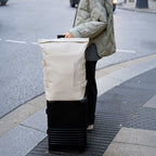 Lieblingstasche Helsinki Pro beige rolltop backpack resting on a black suitcase on a city street