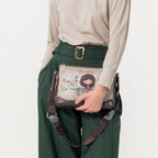 Lieblingstasche cross-body bag with illustrated girl graphic, worn by a woman in a beige long-sleeve top and green pants