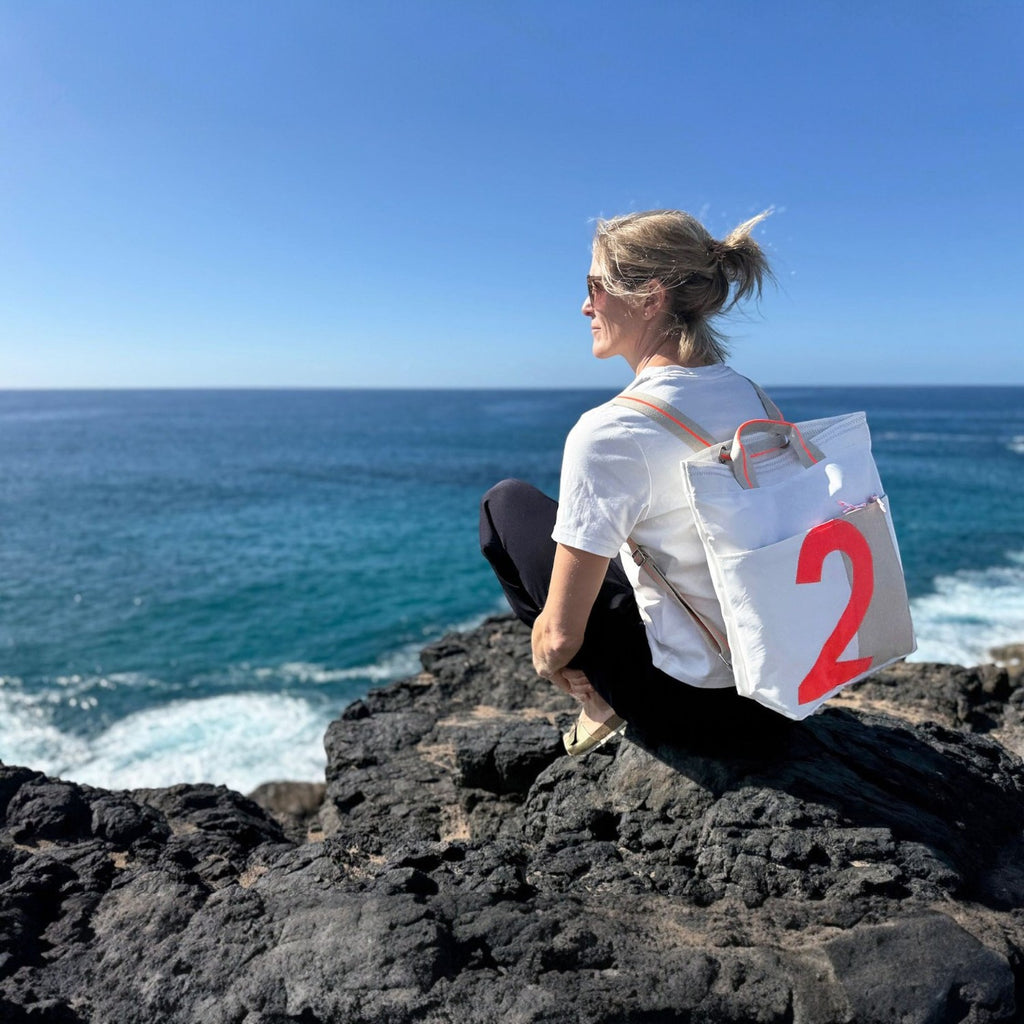 Lieblingstasche Kaje white canvas backpack with large red number 2 graphic, worn by a woman on a rocky coast.