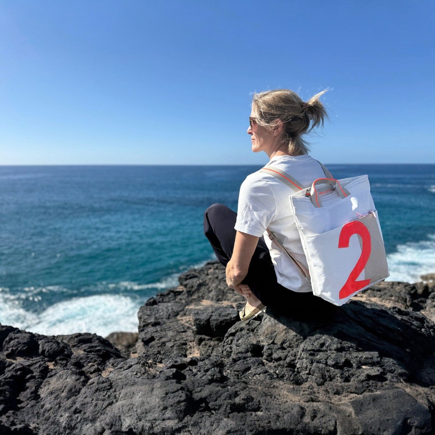 Lieblingstasche Kaje white canvas backpack with large red number 2 graphic, worn by a woman on a rocky coast.