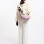 Model wearing a large dusty pink Lieblingstasche Moon Bag Ruffle with a crescent shape over a cream jacket and pants.