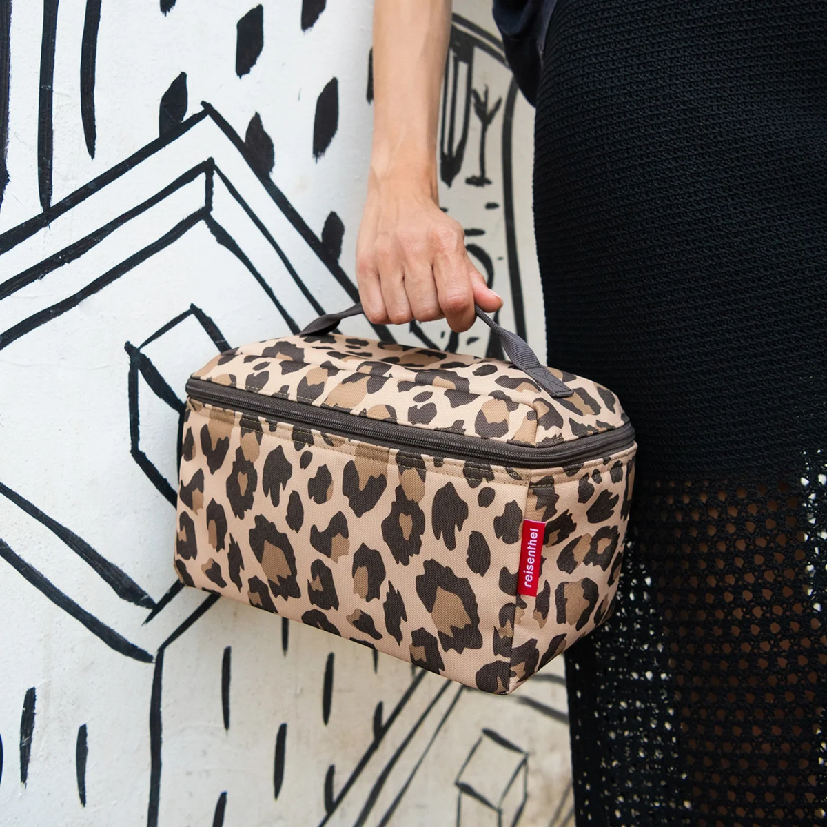 Lieblingstasche leopard print beauty case with top handle held by a person against a black and white mural background